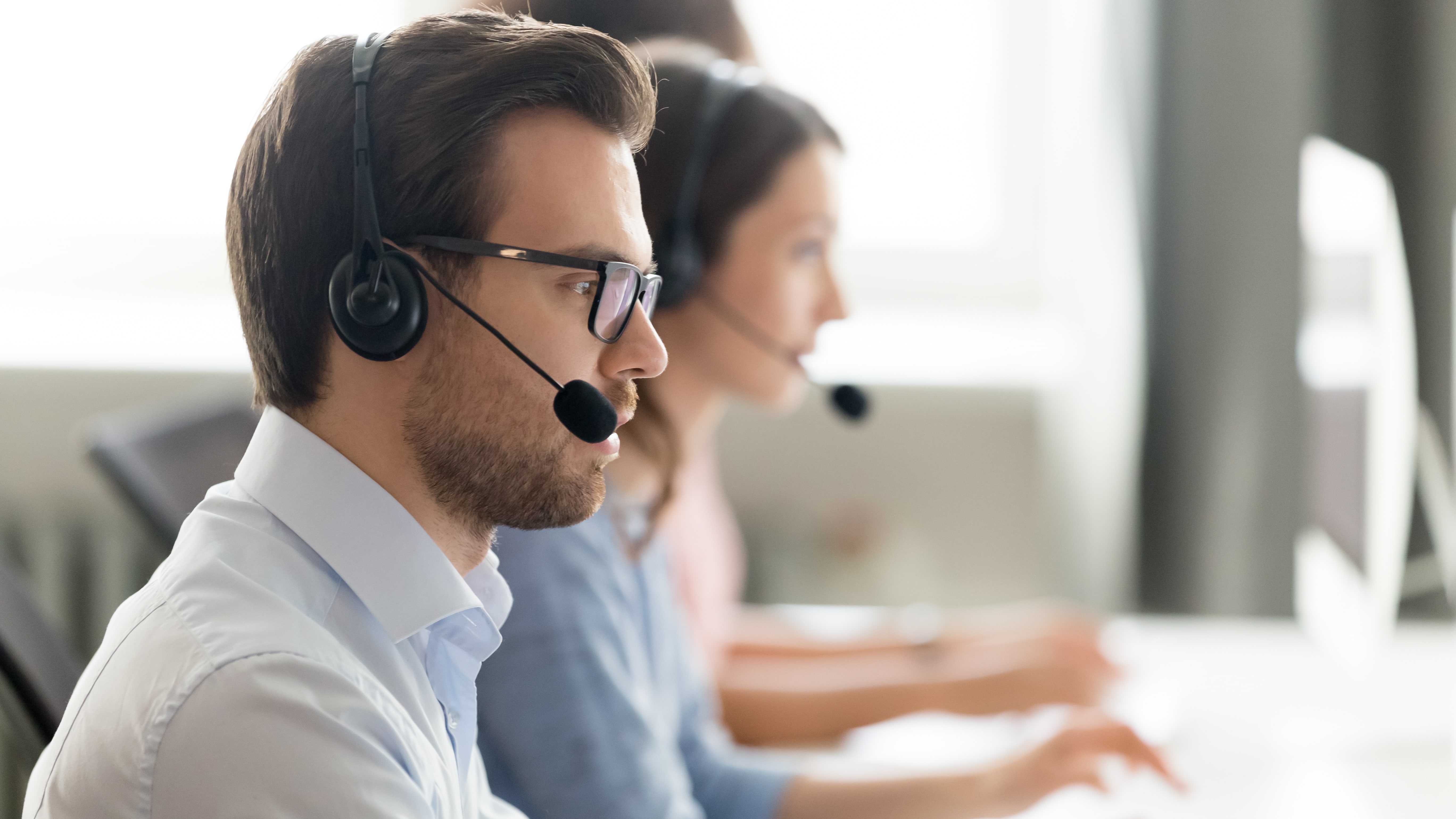 Customer service representatives wearing headsets working at computers in a call center.